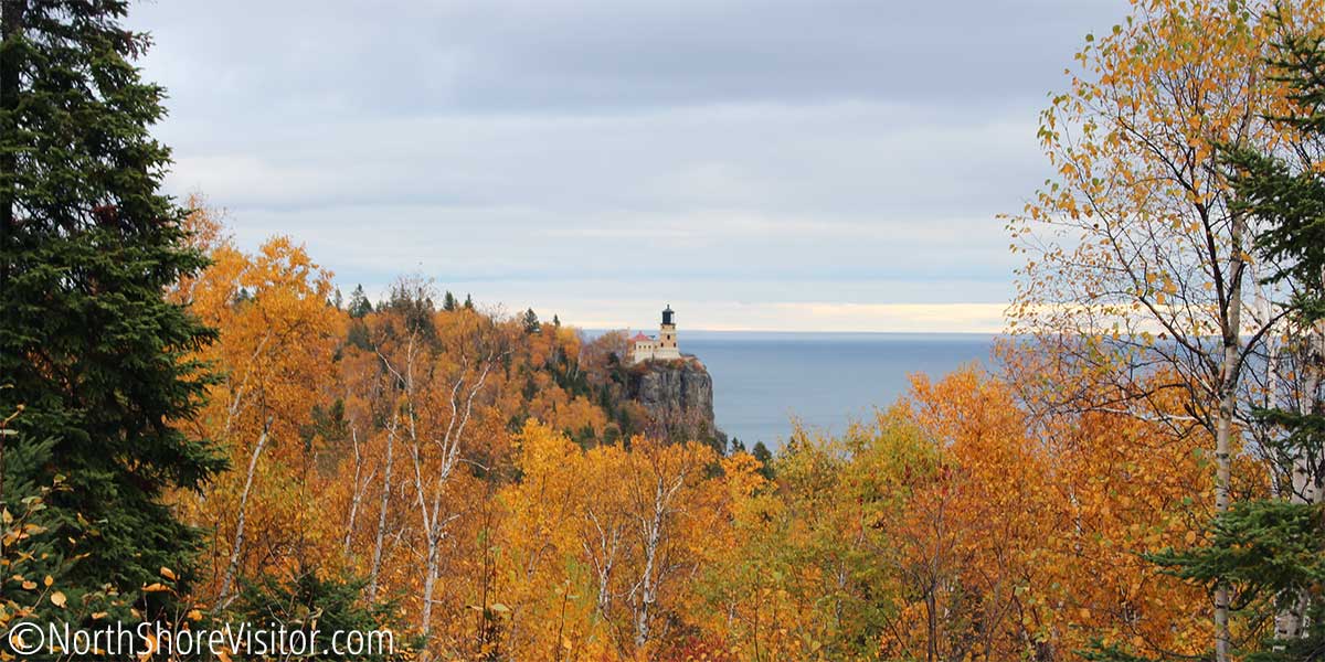 looking over gold and orange treetops at split rock lighthouse in the fall