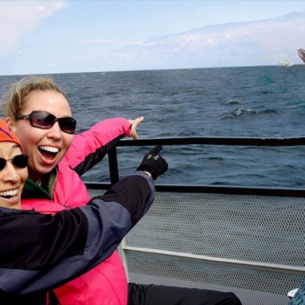 two excited women point out whale jumping from lake superior