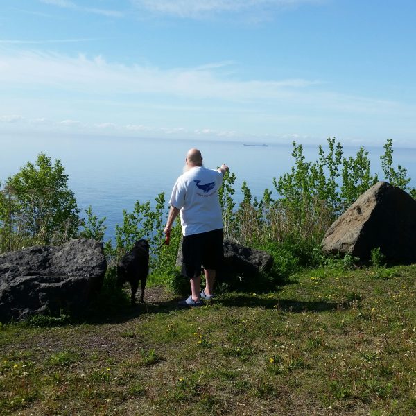 man in whale watching t-shirt and lab on lake superior shore