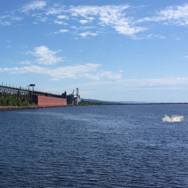 splash from a whale on lake superior with taconite harbor in the background